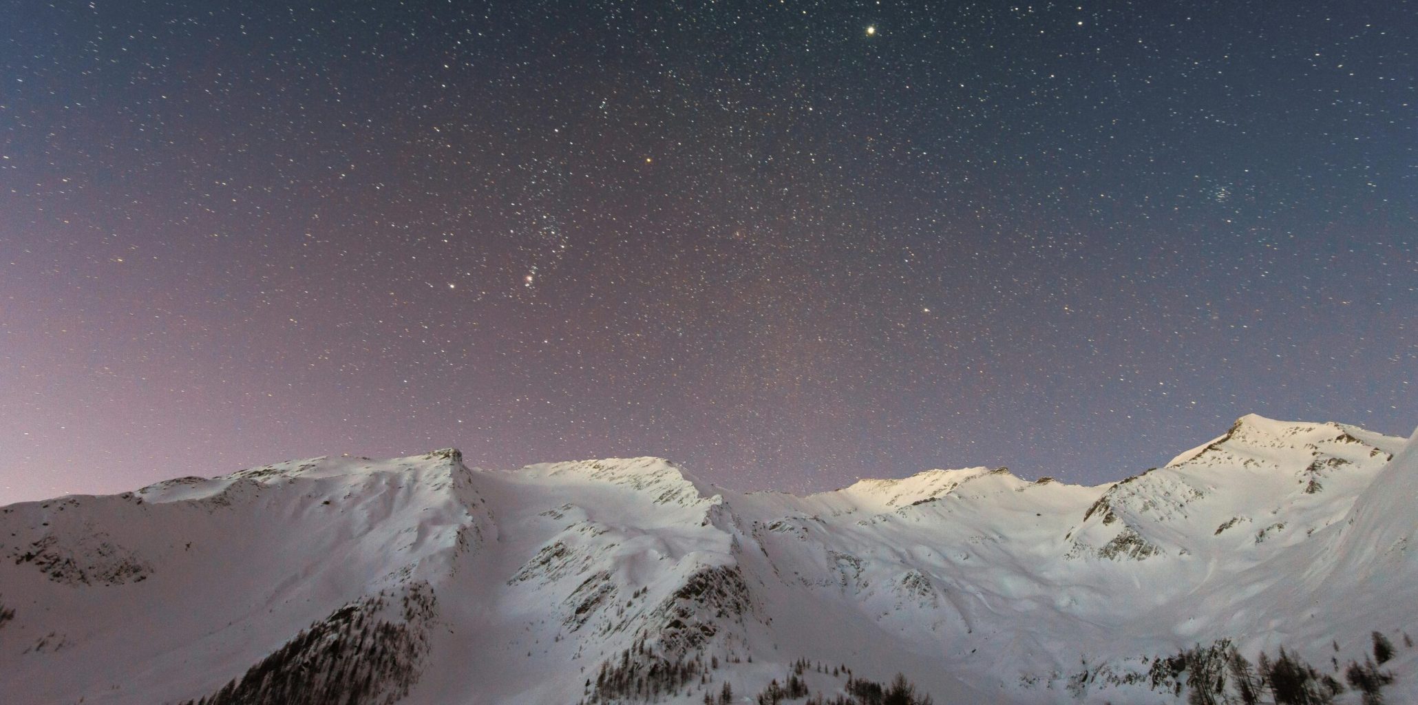 A breathtaking view of snow-capped mountains under a starry night sky, capturing the beauty of winter outdoors.