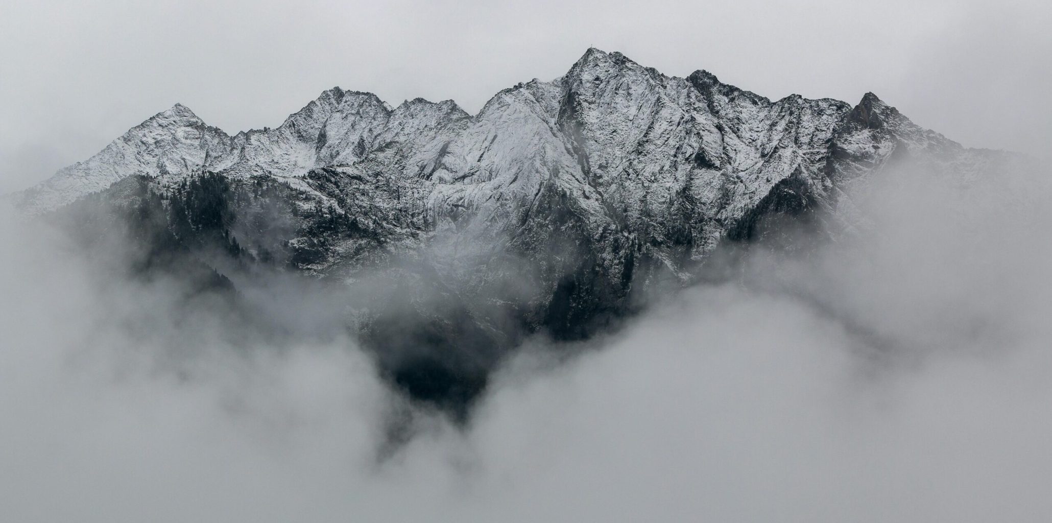 A breathtaking view of snow-covered mountain peaks surrounded by dense fog, creating a mystical landscape.